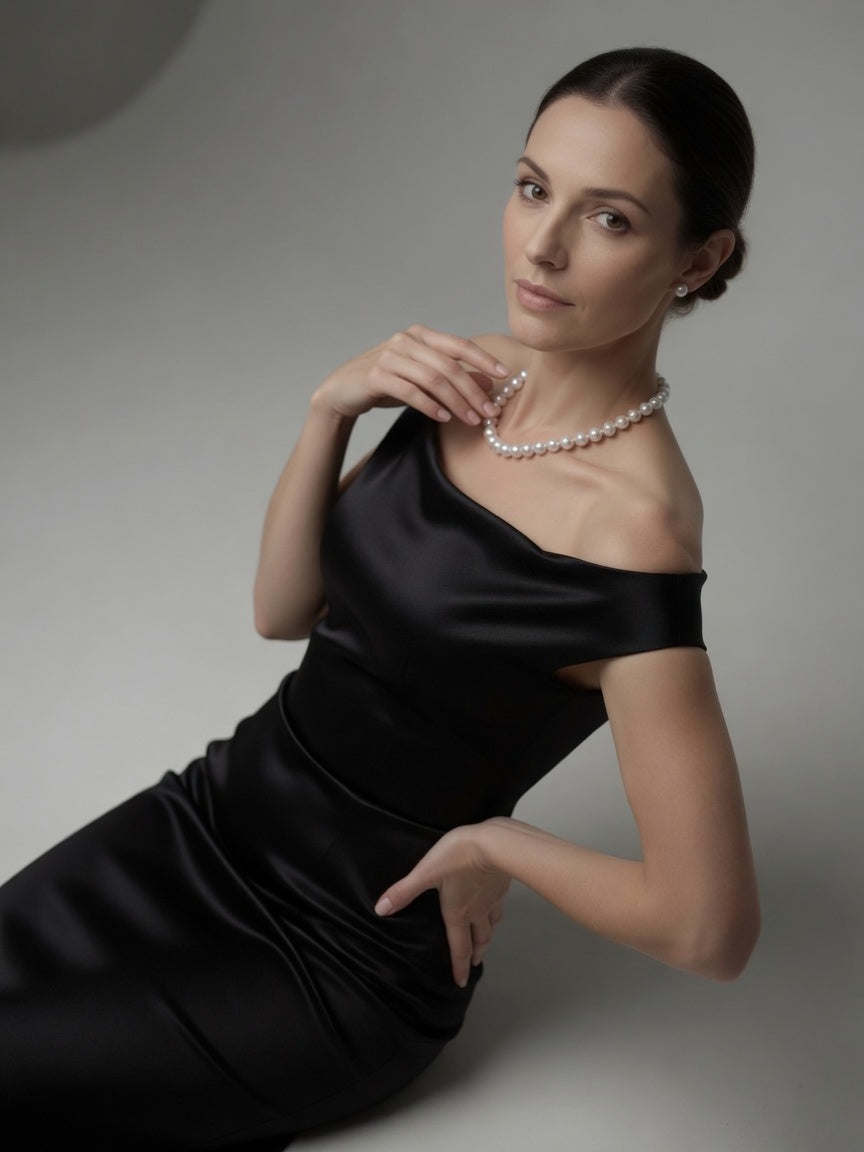 Woman wearing a black dress and pearl necklace against a gray background